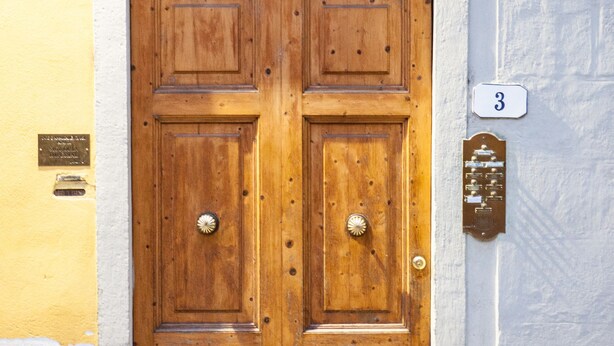 Uma porta dupla de madeira com uma grade metálica acima, uma placa com o número 3 e uma pequena placa na parede à esquerda.