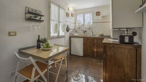 Uma cozinha compacta com mesa de madeira, cadeiras brancas, uma pequena geladeira e um armário de madeira.