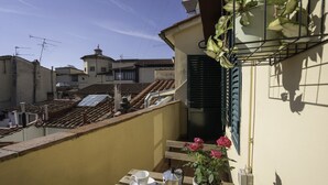Varanda com mesa posta para dois, planta em vaso e vista para edifícios vizinhos.