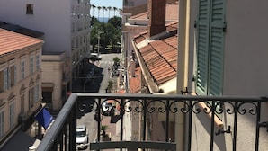Blick von einem Balkon auf eine Straße mit Gebäuden, einem klaren Himmel und einem Straßenschild.