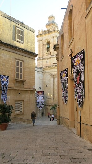 Una estrecha calle con edificios históricos, una torre de campanas y banderines decorativos.