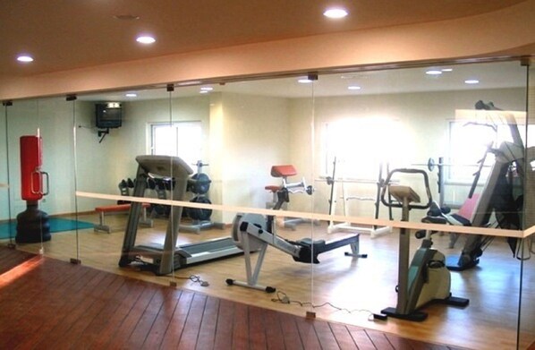Un gimnasio con equipo de ejercicio, una cinta de correr y un espejo que refleja la sala.