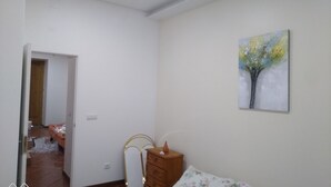 Ein Schlafzimmer mit Bett, Schminktisch, einem Bild an der Wand und einer Tür zu einem anderen Raum.