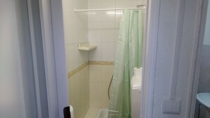 Ein Badezimmer mit Dusche, Toilette und einer kleinen Ablagefläche.