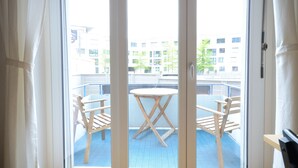 Ein Balkon mit rundem Tisch und zwei Stühlen, mit Blick auf ein Gebäude mit vielen Fenstern.
