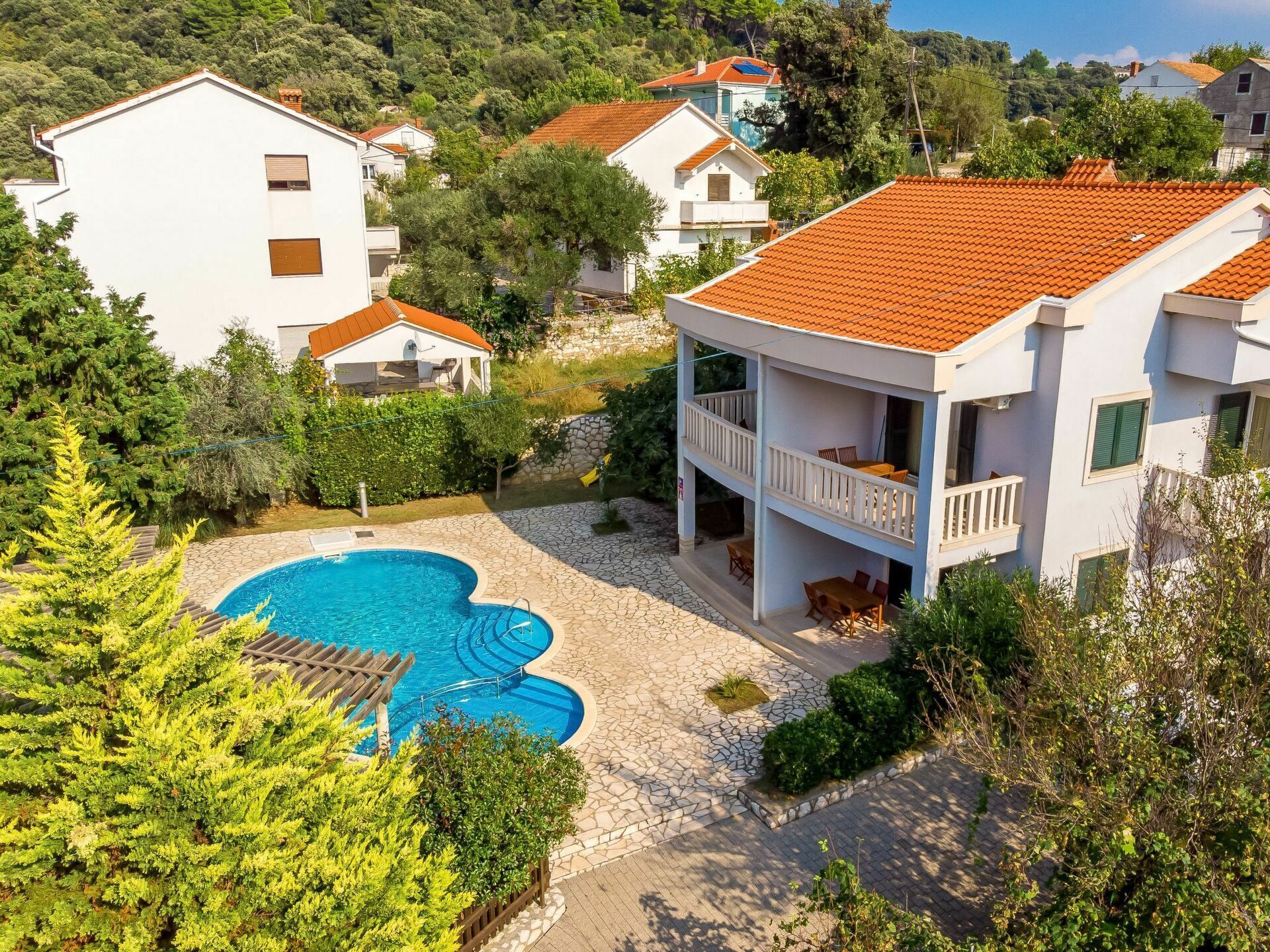 A residential building with a swimming pool, surrounded by greenery and other houses.