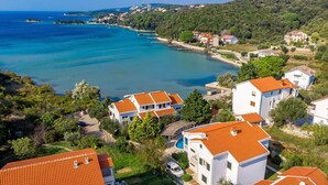 Un quartier résidentiel en bord de mer, avec des maisons aux toits recouverts de tuiles rouges, entourées de verdure et bordé par une mer d’un bleu limpide.