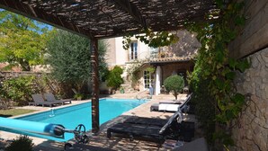 Un área de piscina con sillones de descanso y una pérgola.