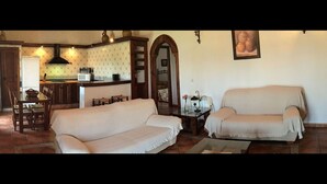 A living room with two sofas, a dining table with chairs, a kitchen area with a stove and microwave, and a framed picture on the wall.