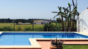 A swimming pool with lounge chairs, surrounded by a fence and greenery, with houses in the background.