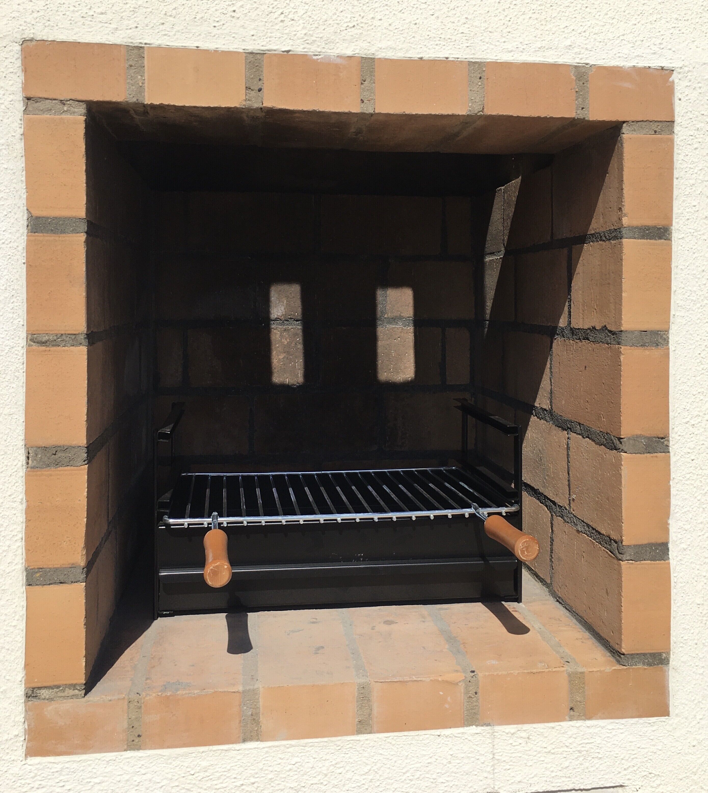 Een barbecue van baksteen met een metalen rek en houten handgrepen.