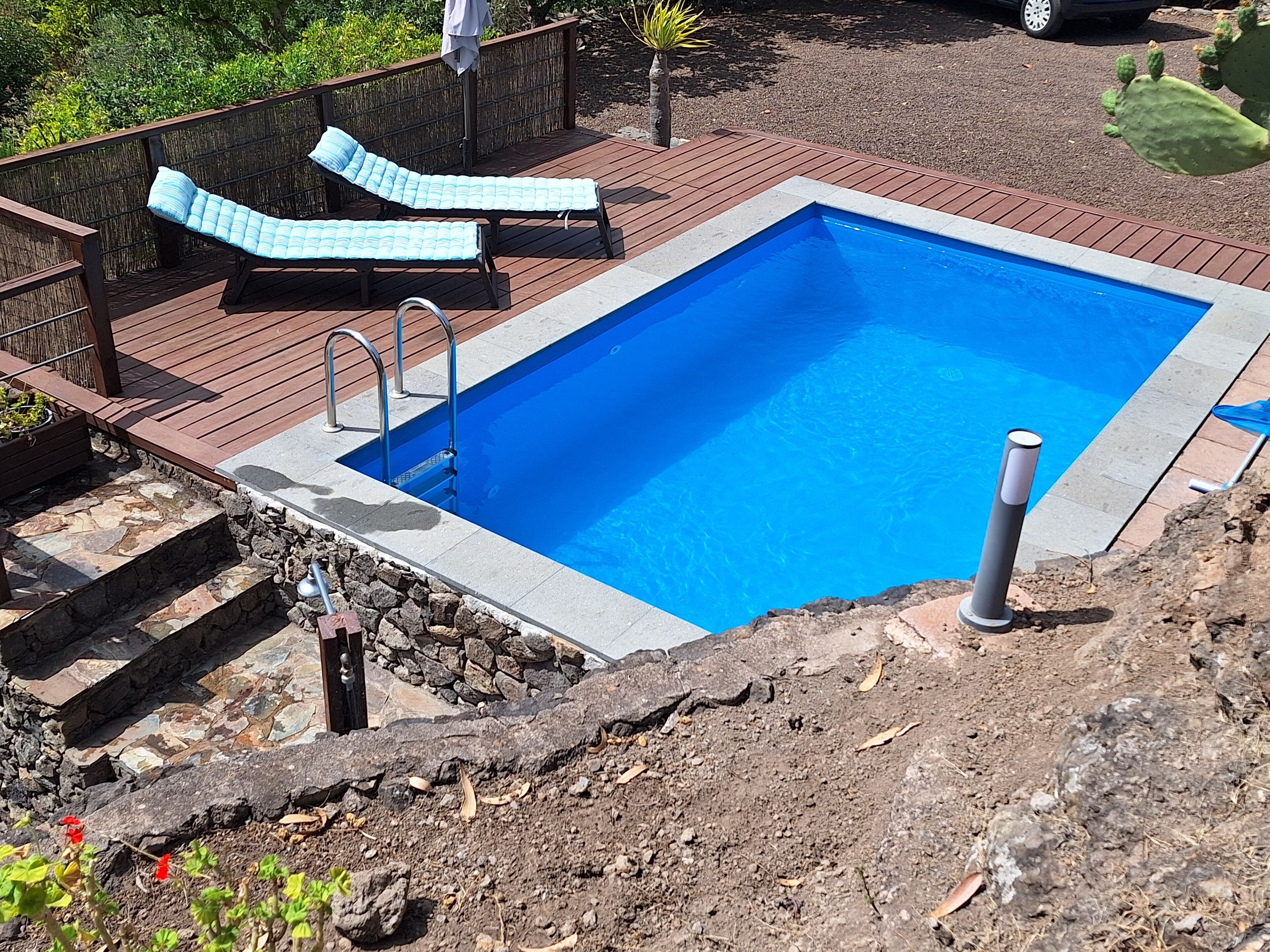 A rectangular swimming pool with a stone border, surrounded by a wooden deck with lounge chairs.