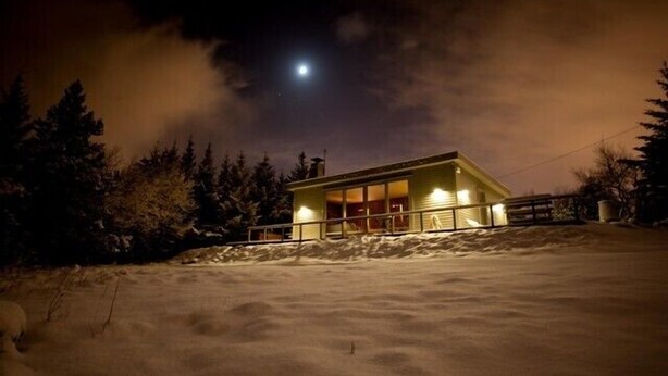 A snow-covered landscape with a single-story building illuminated by interior lights.