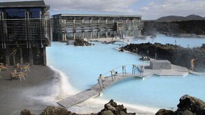 A geothermal spa with pools, a wooden deck, and a modern building with large windows.