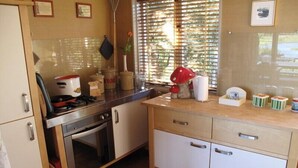 A kitchen with a stove, oven, and cabinets. There is a window with blinds, a plant, and a red mushroom decoration.