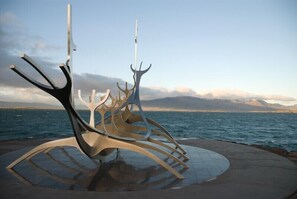 Eine moderne Skulptur am Wasser mit Bergen im Hintergrund.