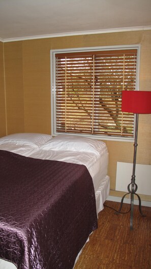 Ein Schlafzimmer mit Bett, Fenster mit Jalousien, einer roten Lampe und einer Heizung.