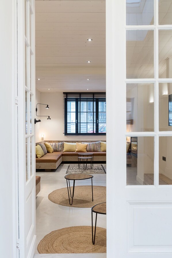 Un salon spacieux avec une grande fenêtre, un canapé avec des coussins, une table basse et un tapis.