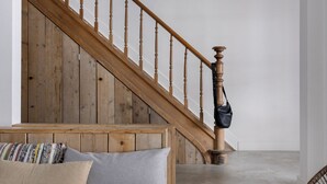 Una escalera de madera con barandilla, un sofá gris con cojines y una silla de mimbre.