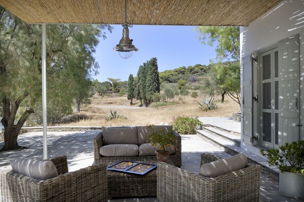 Un área de estar al aire libre techada con mobiliario de mimbre, una lámpara colgante y vistas a un paisaje natural.