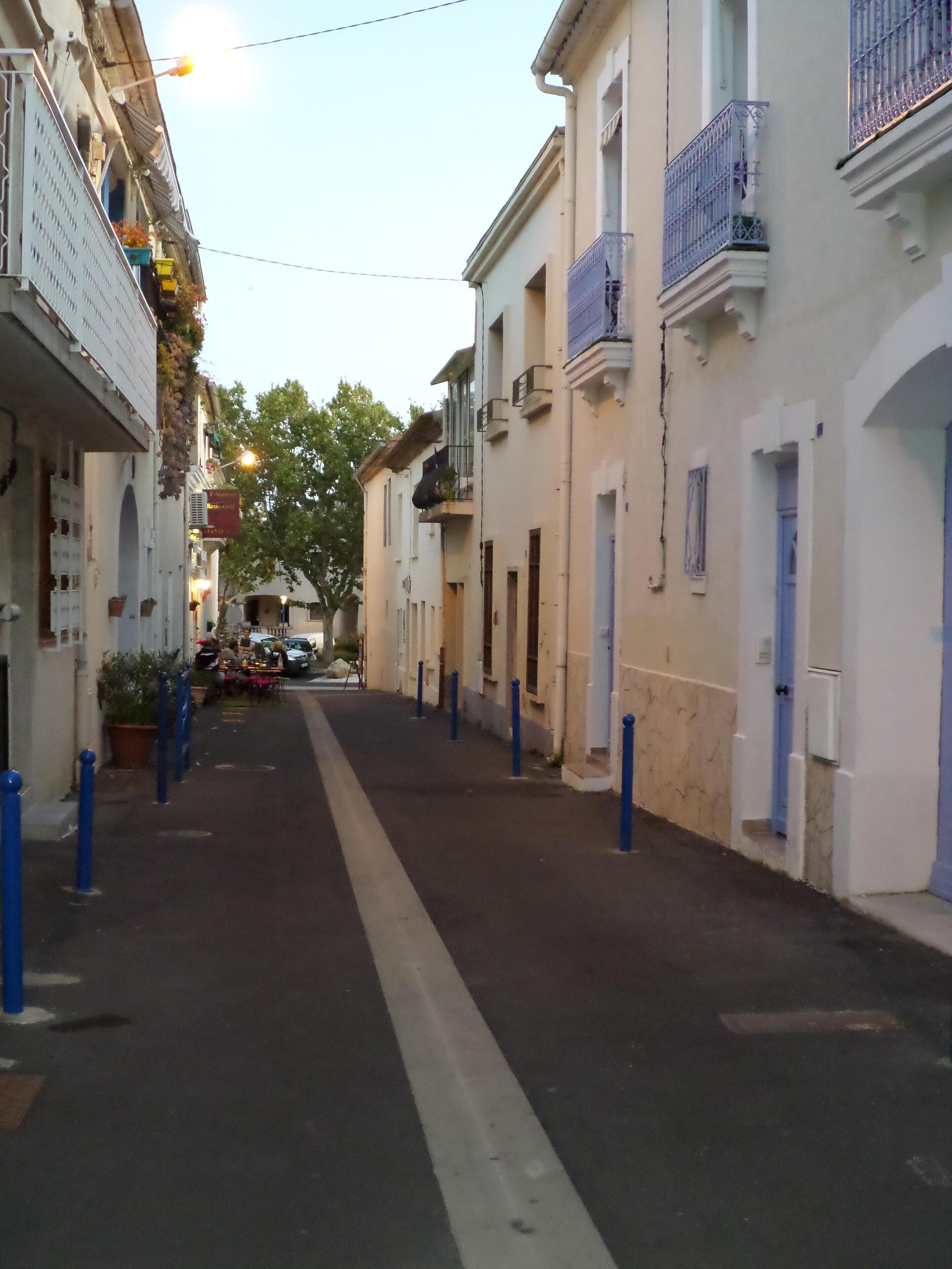 Une rue étroite bordée d’immeubles, certains dotés de balcons et d’autres avec des entrées au niveau du sol.