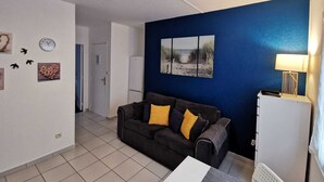 A living room with a dark brown sofa, a white coffee table, and a blue accent wall. - 1-room apartment for spa guests and vacationers (Balaruc-Les-Bains)