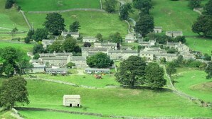 A rural village with stone houses, a central building with a large door, and surrounding fields. - Beautifully Converted Barn With Stunning Views near Aysgarth (Newbiggin Bishopdale)