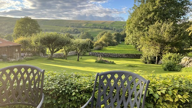 A view from a balcony with chairs, overlooking a well-maintained lawn, stone wall, and trees. - Beautifully Converted Barn With Stunning Views near Aysgarth (Newbiggin Bishopdale)
