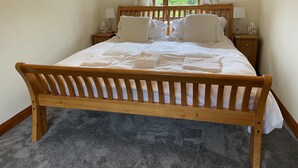 A neatly made bed with white linens and pillows, wooden headboard, two bedside tables with lamps, a window with curtains, and a framed picture on the wall. - Beautifully Converted Barn With Stunning Views near Aysgarth (Newbiggin Bishopdale)