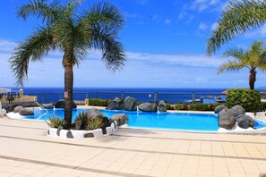 Ein Pool mit Blick auf den Ozean, umgeben von Palmen und Felsen.
