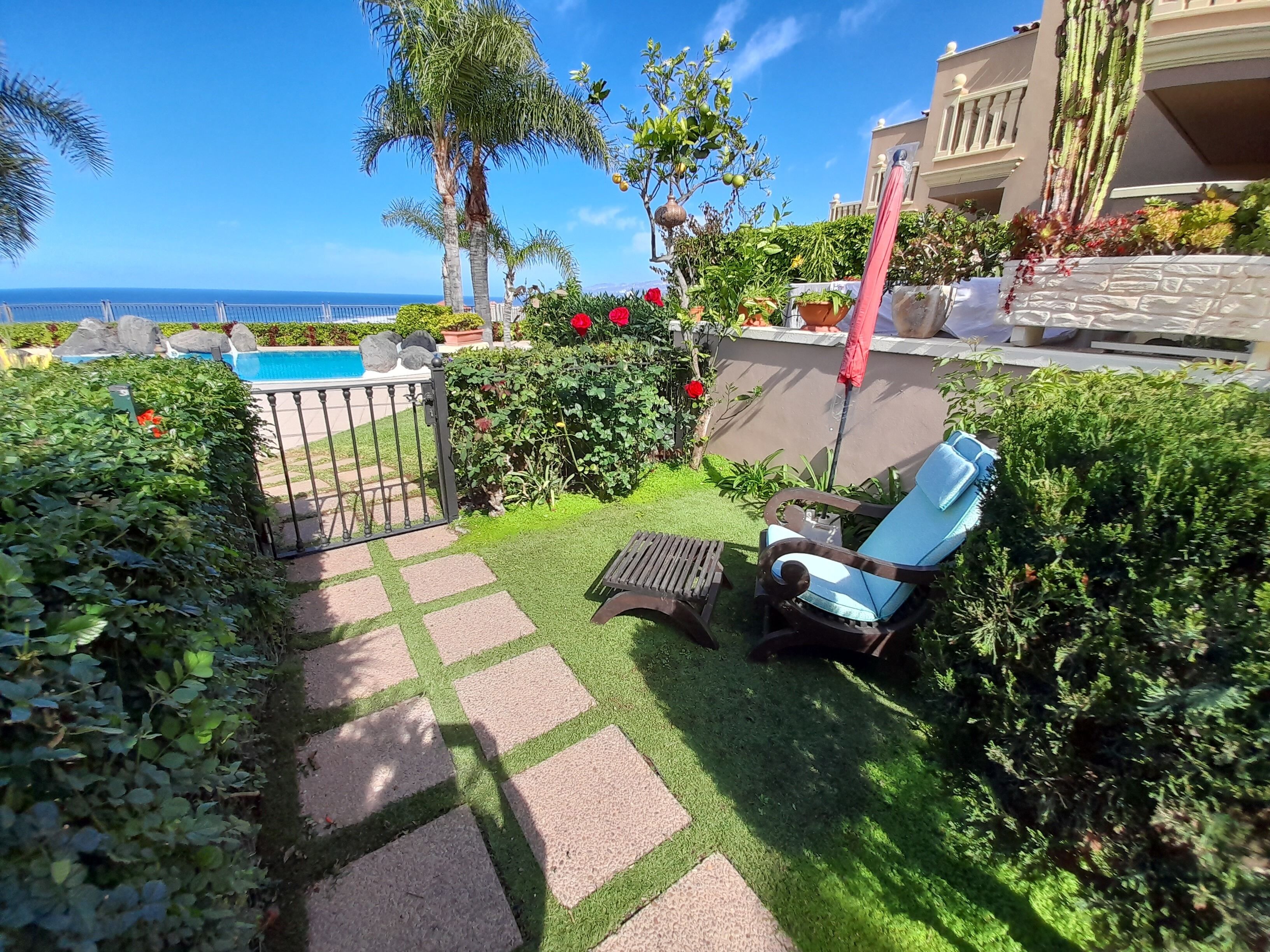 Un espace aménagé au bord de la piscine, avec une chaise et une table, entouré d’une végétation luxuriante et offrant une vue sur l’océan.