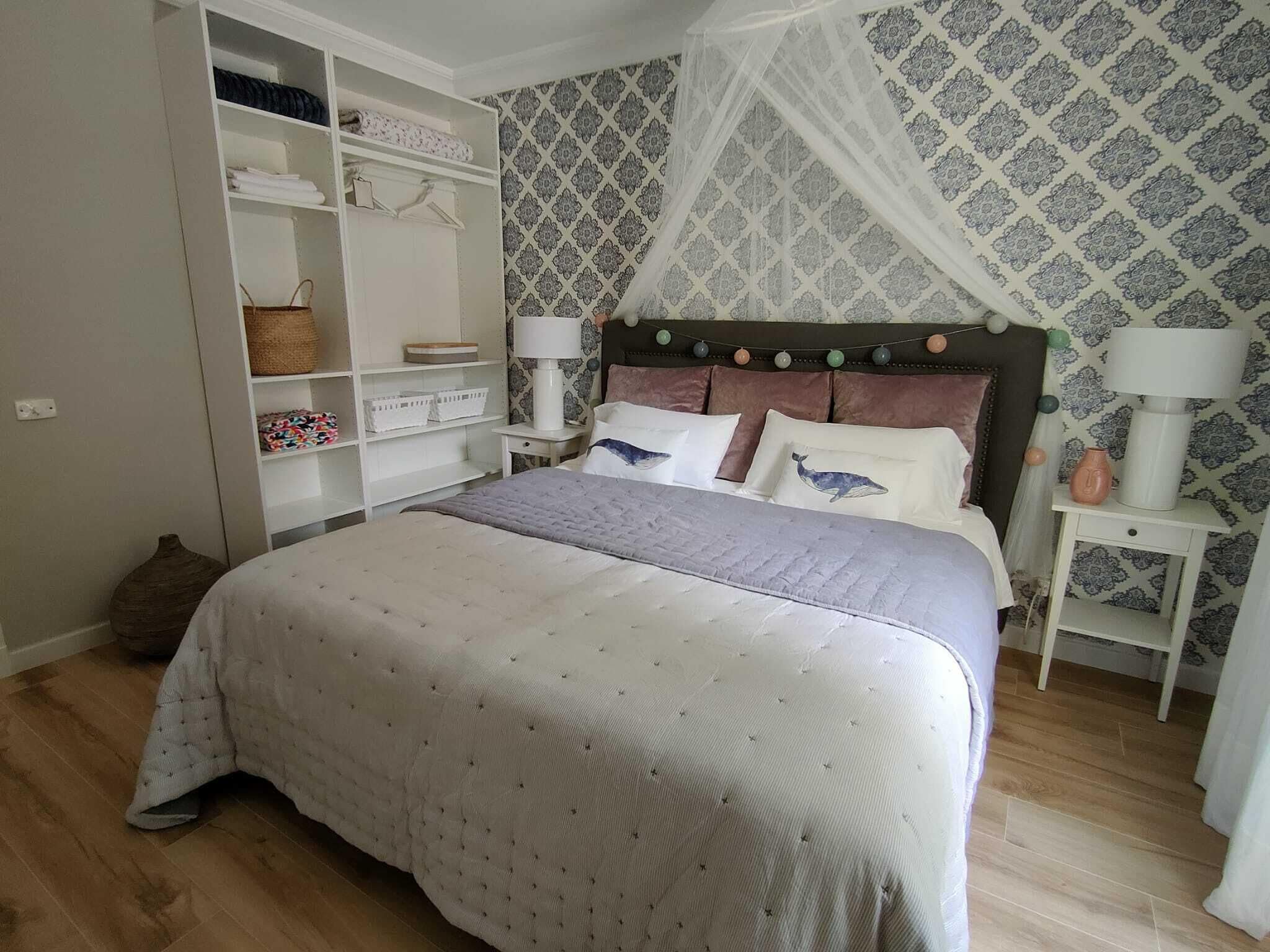 A bedroom with a bed, a wardrobe, a nightstand, and a patterned wallpaper.