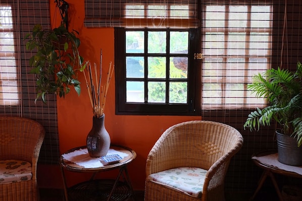 A room with wicker furniture, a window with blinds, and a potted plant.