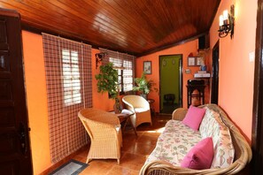 A cozy room with a wooden ceiling, wicker furniture, a sofa with floral cushions, and a green door.