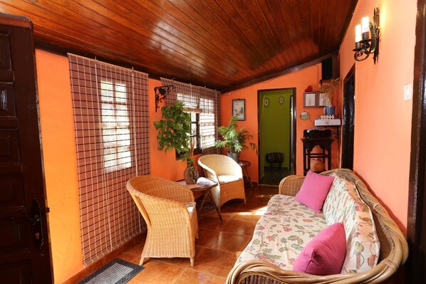 A cozy room with a wooden ceiling, wicker furniture, a sofa with floral cushions, and a green door.