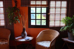 A room with wicker furniture, a window with blinds, and a potted plant.
