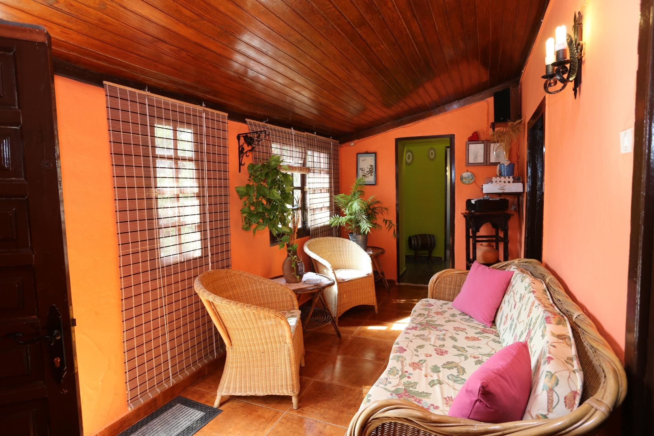 A cozy room with a wooden ceiling, wicker furniture, a sofa with floral cushions, and a green door.