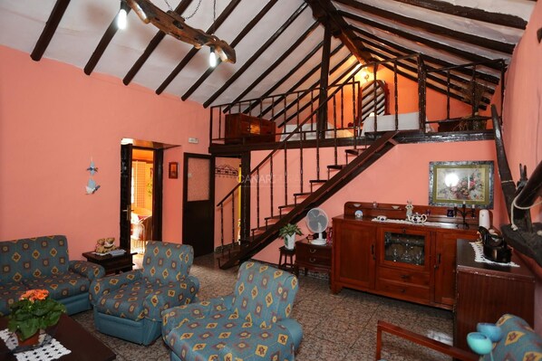 Sala de estar com escada, sofás estampados em azul, mobiliário de madeira e teto com vigas aparentes.