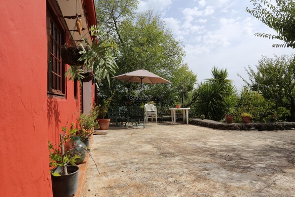 Ein rotes Gebäude mit einer Terrasse, Blumentöpfen, einem Tisch und einem Sonnenschirm.