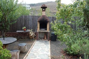 A backyard with a stone pathway leading to a brick-built outdoor oven, surrounded by a wooden fence and greenery.