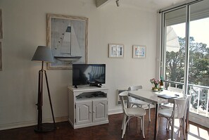 Ein Zimmer mit Fernseher, einer Lampe, einem Esstisch mit Stühlen und Bildern in Rahmen an der Wand.