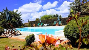 A swimming pool with lounge chairs and umbrellas, surrounded by greenery and a clear sky. - Villa with pool in Tuscany, close to San Gimignano and Volterra  (Villamagna frazione di Volterra)