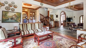 A spacious living room with a wooden ceiling, a large painting, and a traditional sofa. - Zenios Dionysos - Traditional villa overlooking Pindos (Grevena)