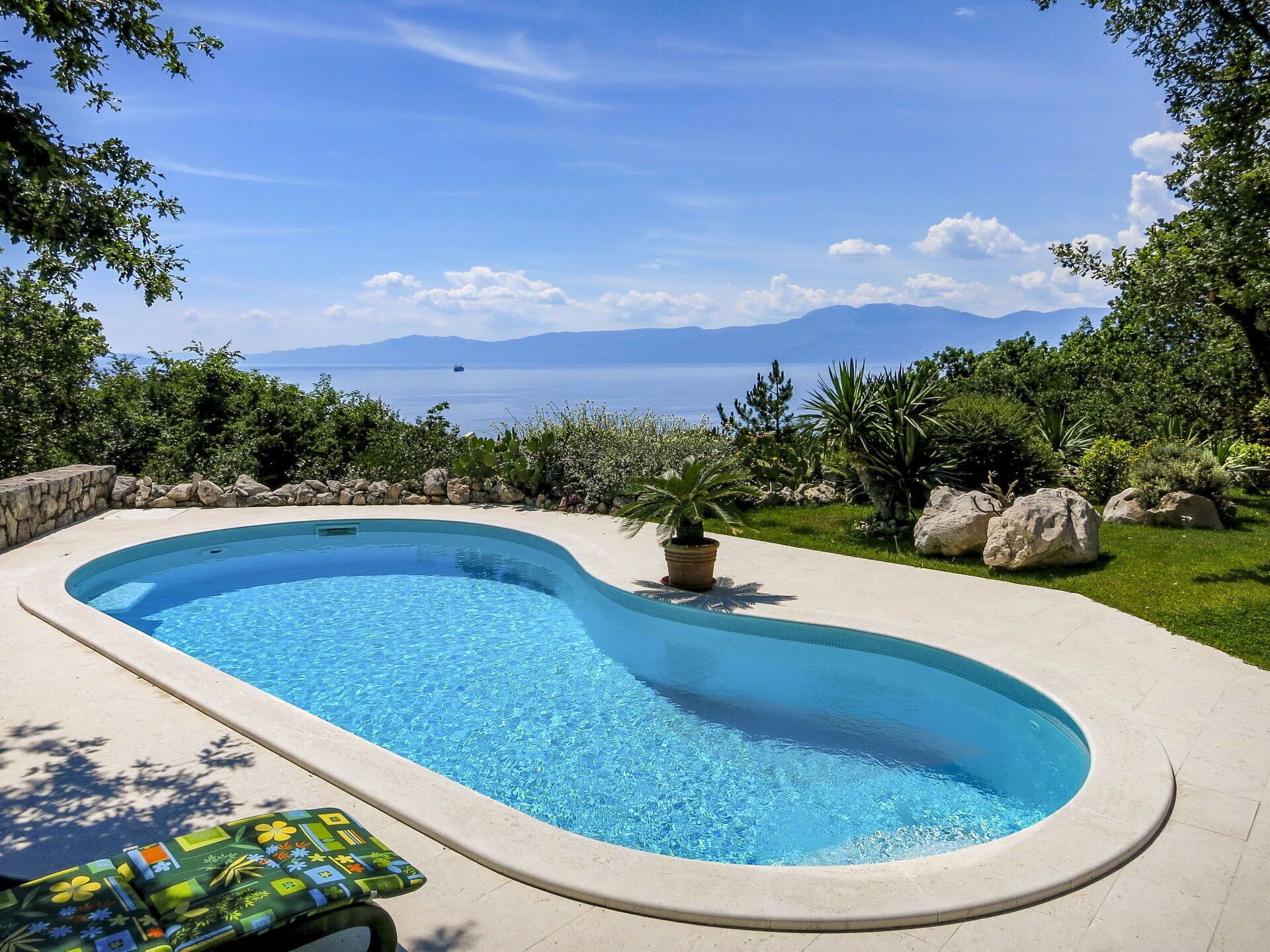 A curved swimming pool with a view of the sea and mountains.