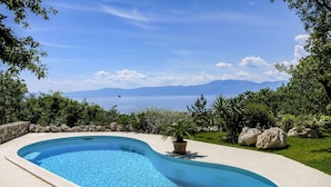 A curved swimming pool with a view of the sea and mountains.