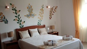 A neatly made bed with a white bedspread and pillows, two bedside tables with lamps, and wall art depicting floral designs. - Private villa with a plunge pool near the beach, featuring 2 large terraces and a hi-fi system (Lagos)