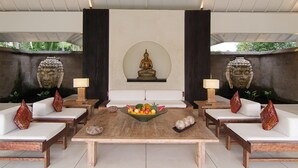 Una habitación con una mesa central rodeada por cuatro sillas blancas acolchadas, una estatua de Buda en el centro y dos grandes esculturas de piedra a cada lado.