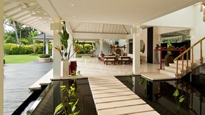 Amplio espacio interior con una escalera de madera, una zona de estar central y una fuente de agua.
