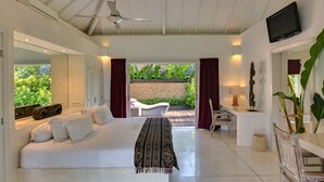 Un dormitorio amplio con una cama grande, ventilador de techo, televisión y vista a un jardín.