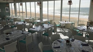 Ein Restaurant direkt am Strand mit Terrassensitzplätzen, großen Fenstern mit Meerblick und rustikalem Interieur.